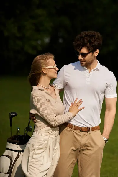 Um homem e uma mulher elegantes em trajes elegantes posam em um campo de golfe exuberante, exalando sofisticação e lazer. — Fotografia de Stock
