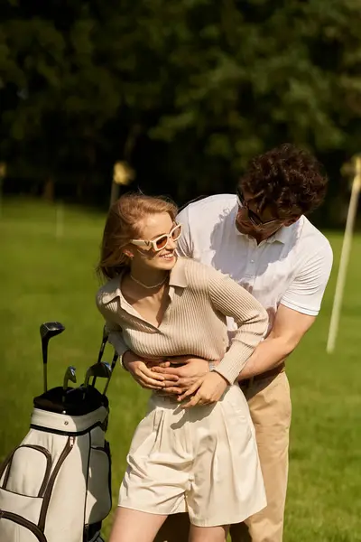 Um jovem casal em trajes elegantes compartilham um abraço caloroso em um campo de golfe intocado, cercado pela beleza da paisagem verde. — Fotografia de Stock