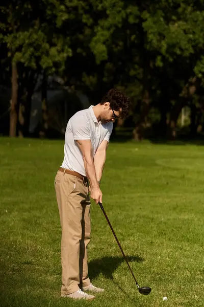 Un hombre con elegante atuendo balanceando un club de golf, golpeando una pelota en un exuberante parque verde, disfrutando de una actividad deportiva de lujo. - foto de stock