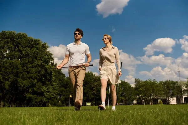 A stylish young couple in elegant attire strolls through a lush green grassy field in a golf club setting. — Stock Photo