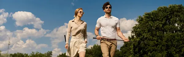 Un jeune couple en vêtements élégants marche sur un parcours de golf luxueux, profitant de l'atmosphère raffinée. — Photo de stock