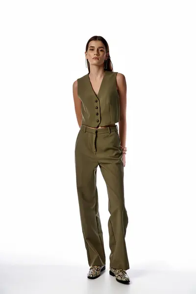 A beautiful woman with long dark hair, dressed in a green jumpsuit, striking a pose against a gray backdrop. — Stock Photo