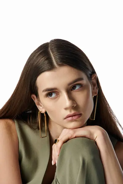A stylish, elegant woman with beautiful long brown hair and gold earrings posing against a gray backdrop. — Photo de stock