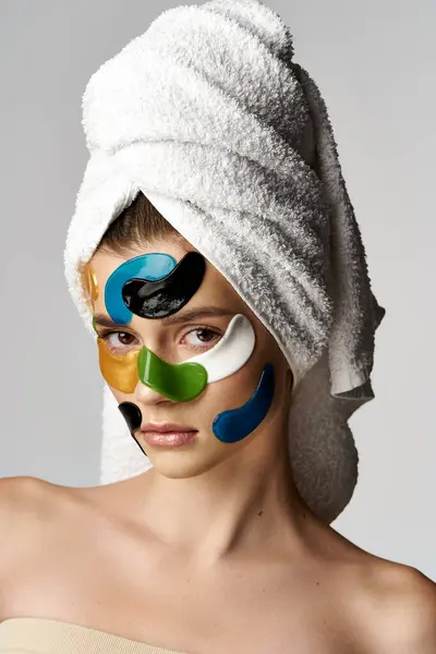 Una mujer joven embellecida con parches para los ojos se relaja con una toalla envuelta alrededor de su cabeza en un entorno de spa. - foto de stock