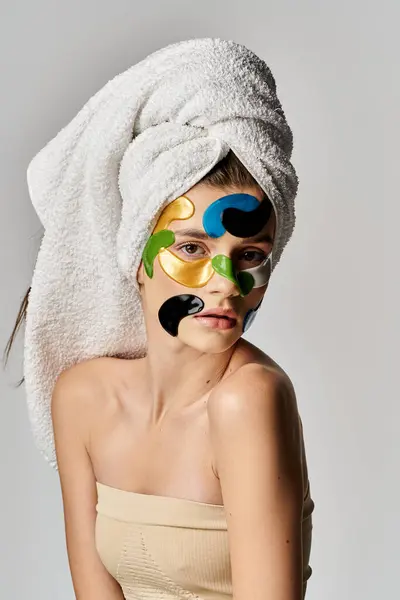 Una hermosa joven, adornada con parches para los ojos y maquillaje, posa confiadamente con una toalla envuelta alrededor de su cabeza como un turbante. - foto de stock