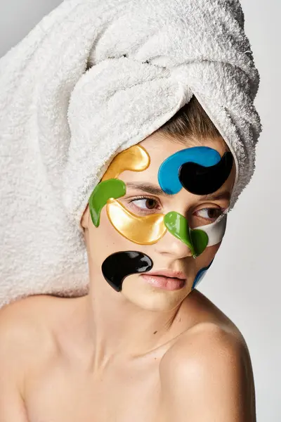 Atractiva mujer joven con una toalla envuelta alrededor de su cabeza y parches para los ojos. - foto de stock