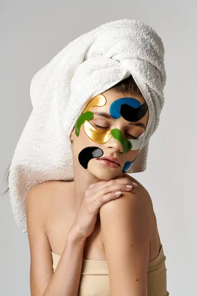 Une femme sereine portant des bandeaux oculaires et une serviette sur la tête, se livrant à une routine relaxante d'autosoin. — Photo de stock