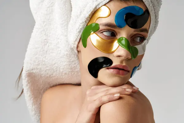 Eine Frau mit einem Handtuch auf dem Kopf trägt Augenklappen, während sie sich mit Make-up-Accessoires selbst pflegt. — Stockfoto