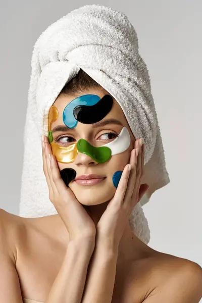 Una joven muestra su belleza con una toalla en la cabeza y con manchas en los ojos en la cara, exudando elegancia y encanto. - foto de stock