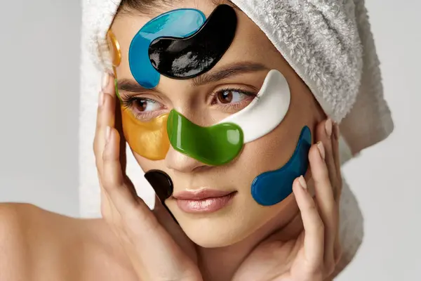 Молода жінка з рушником на голові та очних латках, демонструє красу та процедури догляду за собою. — стокове фото