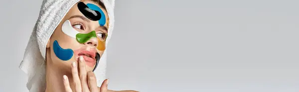 Una hermosa joven con una toalla envuelta alrededor de su cabeza, con parches en los ojos. - foto de stock