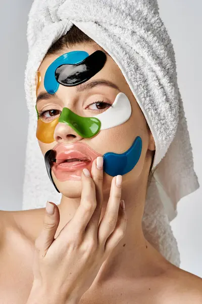 Una joven impresionante con una toalla envuelta alrededor de su cabeza con manchas en los ojos en su cara, realzando su belleza natural. - foto de stock