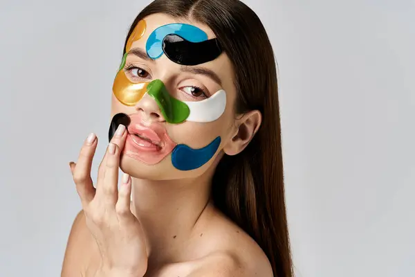 Молодая женщина с повязками на лице, демонстрирующая красочный и творческий макияж с смелыми красками и преувеличенными чертами лица. — стоковое фото