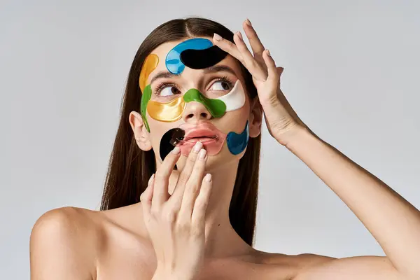 Une jeune femme avec des patchs sur le visage lève les mains, mettant en valeur son maquillage artistique et sa beauté. — Photo de stock