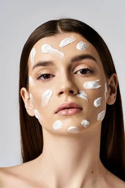 Una bella giovane donna con crema bianca sul viso, creando un'immagine lussuosa e serena. — Foto stock