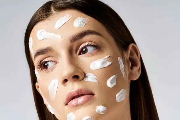 Una hermosa joven con mucha crema en la cara, mostrando su rutina de cuidado de la piel. - foto de stock