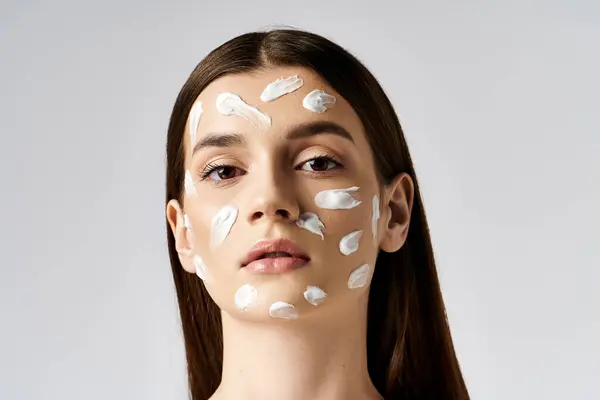 Красивая молодая женщина элегантно демонстрирует щедрое количество крема на лице, демонстрируя роскошные процедуры по уходу за кожей. — стоковое фото
