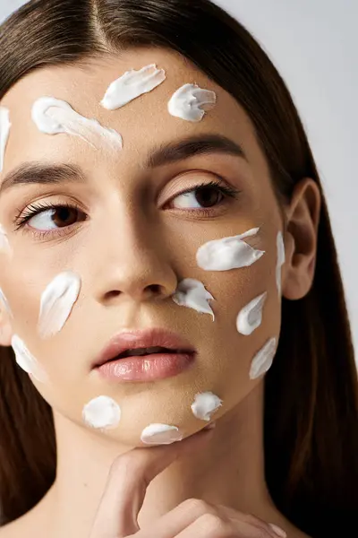 Красивая молодая женщина позирует с большим количеством крема на лице, наслаждаясь рутиной по уходу за кожей для сияющего лица. — стоковое фото