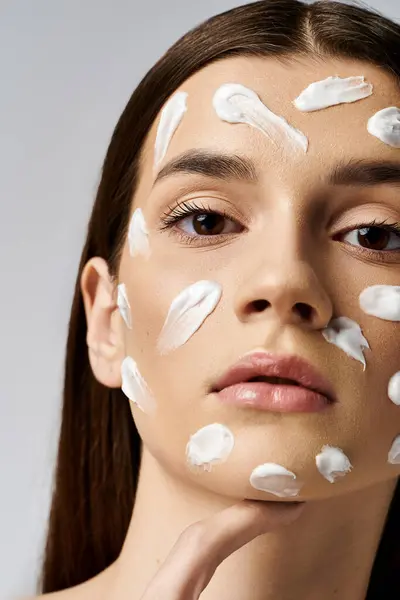 Une jeune femme orne son visage d'une luxueuse quantité de crème blanche, rayonnant d'un éclat serein et éthéré. — Photo de stock