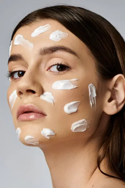 Eine schöne junge Frau mit einer Fülle von Creme im Gesicht, die eine luxuriöse Hautpflege-Routine zeigt. — Stockfoto