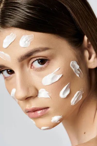 Una bella giovane donna con una generosa quantità di crema sul viso, indulgendo in una routine di cura della pelle. — Foto stock