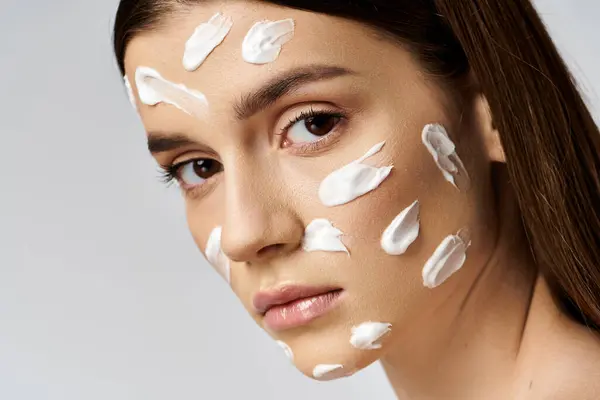 Une jeune femme avec une généreuse quantité de crème sur le visage est rayonnante et se chouchoute. — Photo de stock