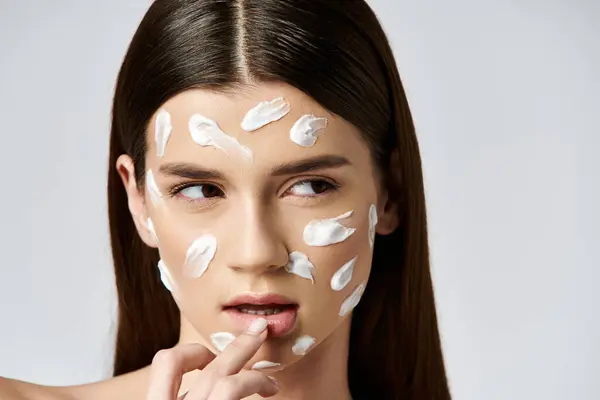 Une jeune femme avec une crème blanche sur le visage, mettant en valeur un mélange de beauté et de mystère. — Photo de stock