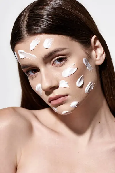 A beautiful young woman posing with white cream on her face, creating a unique and artistic look. — Stock Photo