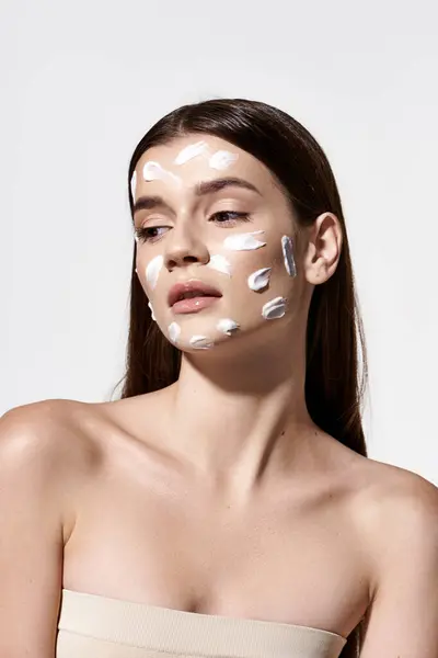 Красивая молодая женщина с белым кремом на лице, демонстрирующая безупречную кожу и вечную элегантность. — стоковое фото