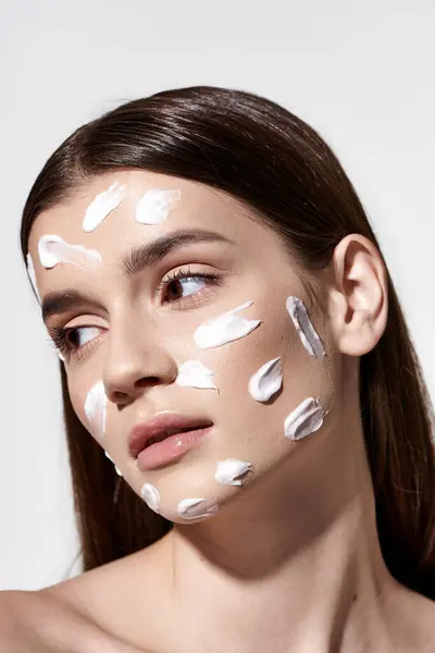 A beautiful young woman poses gracefully with a white cream on her face, exuding an air of mystery and elegance. — Photo de stock