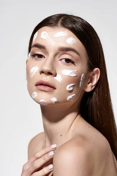 A beautiful young woman elegantly showcases a white cream on her face, adding an air of mystery and allure. — Stock Photo