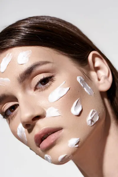 Una bella giovane donna che colpisce una posa indossando una crema bianca sul viso, accentuando la sua bellezza naturale. — Foto stock