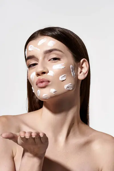 Uma bela jovem mulher vestindo um creme branco em seu rosto, adicionando um elemento de mística e elegância à sua aparência. — Fotografia de Stock