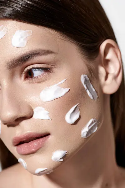 Una joven impresionante con una generosa cantidad de crema blanca aplicada con gracia en su cara, exudando belleza y elegancia. - foto de stock