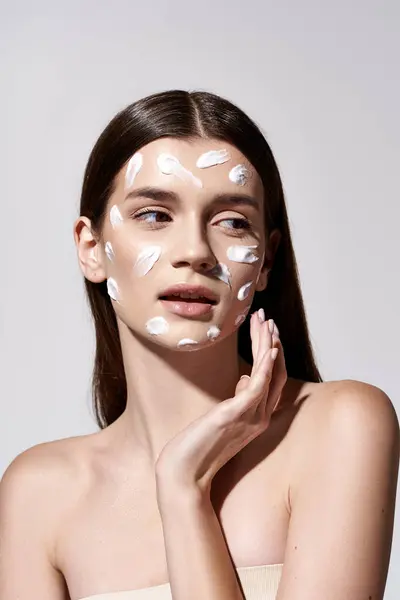 A beautiful young woman delicately wears a white cream on her face, exuding an air of mystery and allure. — Stock Photo