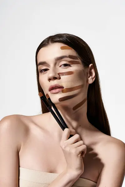 Une jeune femme avec divers pinceaux de maquillage sur le visage, créant un look créatif et artistique avec des fondations. — Photo de stock