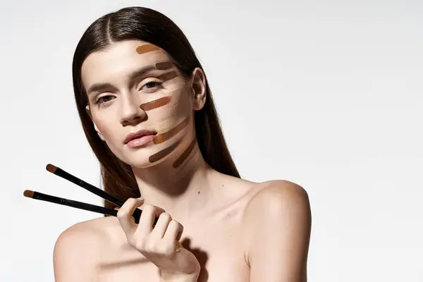 Femme gracieuse avec divers pinceaux de maquillage sur son visage, créant un look créatif et artistique avec des fondations. — Photo de stock