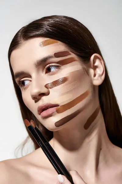 Una mujer delicadamente sostiene dos pinceles de maquillaje frente a su cara, mostrando su rutina de belleza. - foto de stock