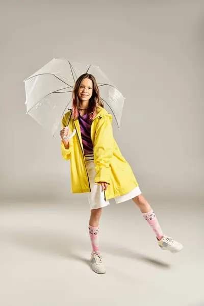 Hermosa adolescente en un impermeable amarillo elegante está posando alegremente, sosteniendo un paraguas colorido en un día lluvioso. - foto de stock