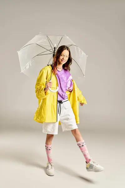 A stylish teenage girl in a yellow raincoat joyfully holds an umbrella, radiating vibrant energy and positivity. — Stock Photo