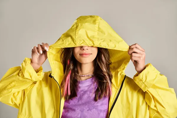 Une adolescente dans un imperméable jaune couvrant son visage avec ses mains dans une pose animée. — Photo de stock