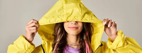 Стильна дівчина-підліток в жовтому плащі, що закриває обличчя руками. — стокове фото