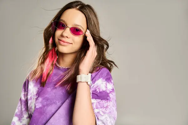 Elegante adolescente posa con confianza en el pelo rosa y la camisa púrpura, vistiendo gafas de sol de moda. - foto de stock