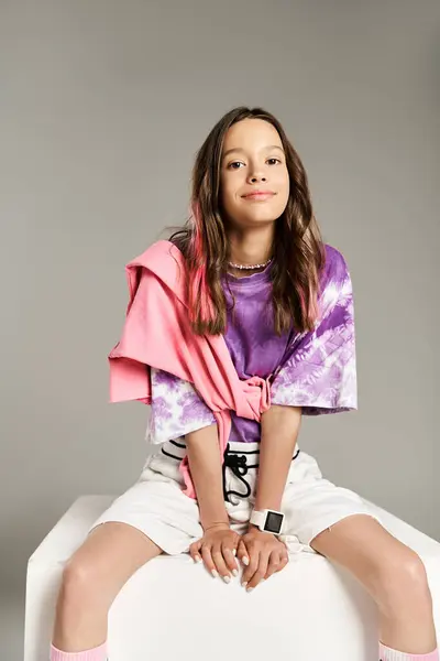 A stunning teenage girl in vibrant attire confidently sits atop a white object. — Stock Photo