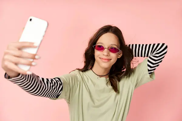 Adolescente élégante en tenue vibrante prend selfie avec téléphone portable, portant des lunettes de soleil fraîches. — Photo de stock