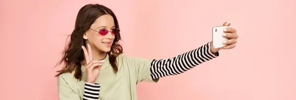Une adolescente à la mode en tenue vibrante prenant un selfie avec son téléphone portable. — Photo de stock