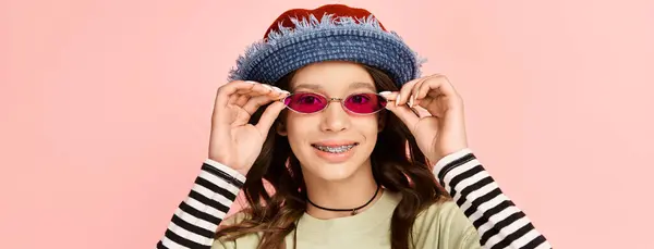 A stylish teenage girl poses confidently in vibrant attire, sporting a trendy hat and sunglasses. — Photo de stock