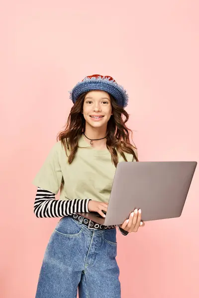 Elegante ragazza adolescente in jeans e un cappello, con fiducia in possesso di un computer portatile. — Foto stock