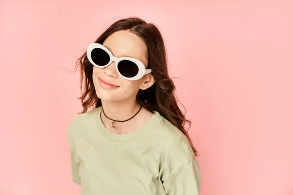 Une petite fille élégante prend une pose en tenue vibrante, berçant une paire de lunettes de soleil rondes avec flair. — Photo de stock