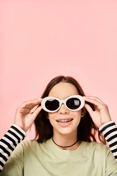 Une adolescente élégante pose avec confiance dans une chemise verte vibrante et des lunettes de soleil blanches à la mode. — Photo de stock